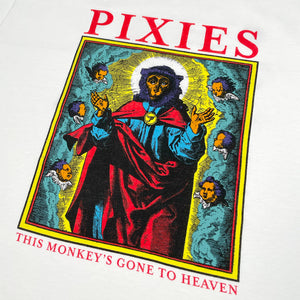 A close up of a white t shirt against a white background with red text reading "Pixies." Below the text is a design of a monkey dressed like a saint surrounded by cherubs and clouds. Below this design there is red text reading "This Monkey's Gone to Heaven"
