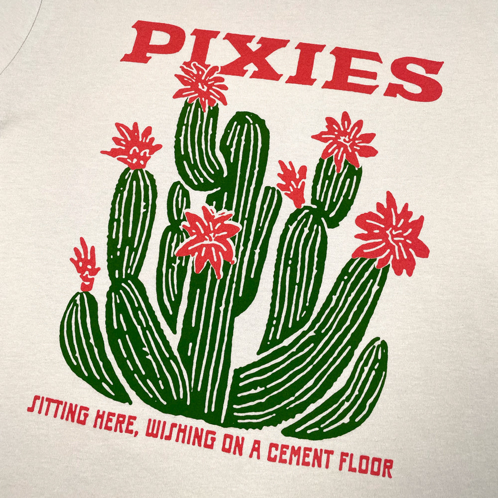 Beige T-Shirt against white background with green and pink graphic displaying a cactus. Pink lettering reads "Pixies, sitting here, wishing on a cement floor"