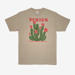 A sand t-shirt featuring a graphic of green cacti with light red flowers and the word 'PIXIES' printed in light red above them and light red text reading "Sitting here, wishing on a cement floor" below. Displayed on a white background.