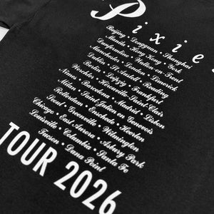 Close-up of white script listing Pixies tour cities, including Dana Point, above Tour 2026 text on black fabric.