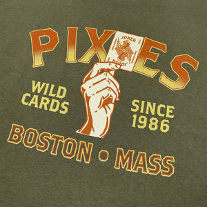 Close up of a military green shirt with yellow and orange text reading "Pixies Wild Cards Since 1986 Boston Mass" with a design of a hand holding a joker playing card.