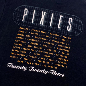 A close up of the back of a black t shirt with white text reading "Pixies" surrounded by a gray grid. Listed below the grid are all 2023 Tour dates, below the cities is white text reading "Twenty Twenty Three"